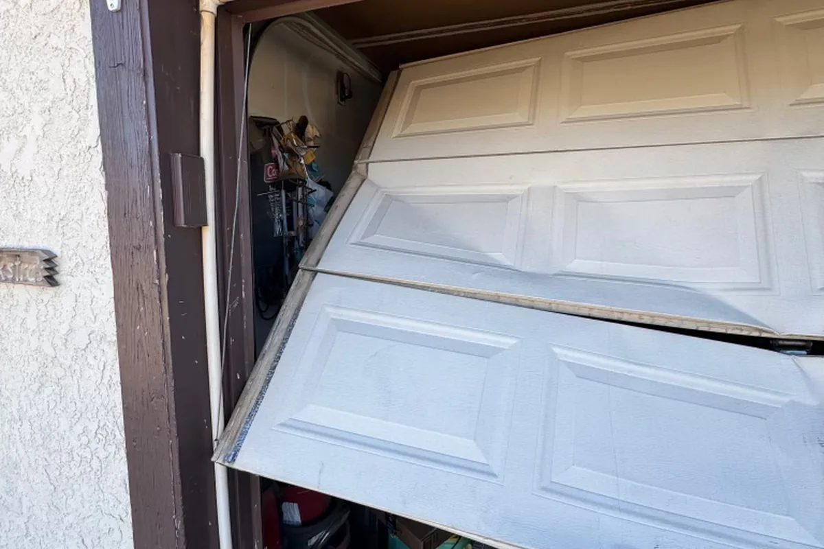 Align Garage Doors repair call: a garage door off its tracks seen from the driveway, panels buckled and stepped out of alignment across the opening